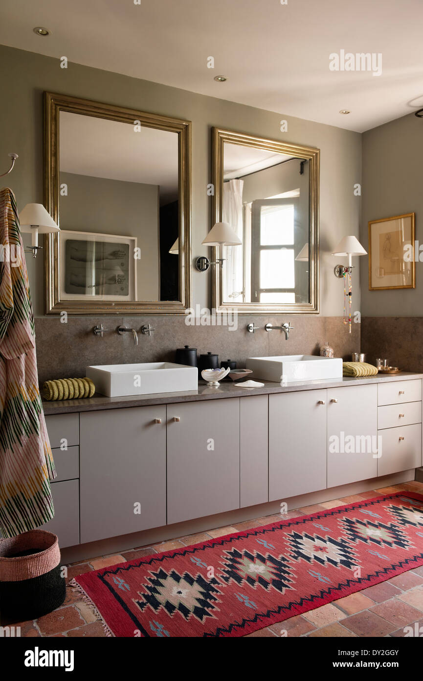 Modern square basins and mirrors in bathroom in grey tones and with ethnic rug. The wall paint is by Emery & Cie Stock Photo