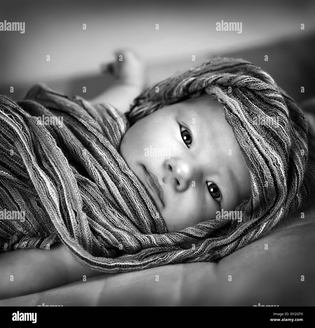 Black and white photo of cute little baby girl wrapped in scarf, lying down on the bed, kids fashion concept Stock Photo