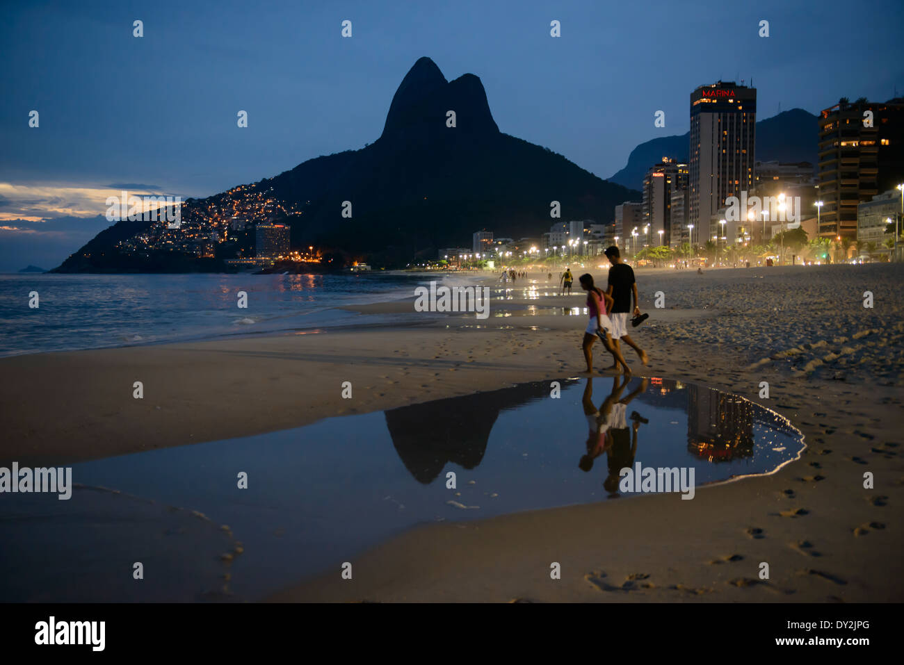 Couple walking along Ipanema beach at night,with twin peaks of Two Brothers mountain at Leblon, in background, Rio de Janeiro, B Stock Photo