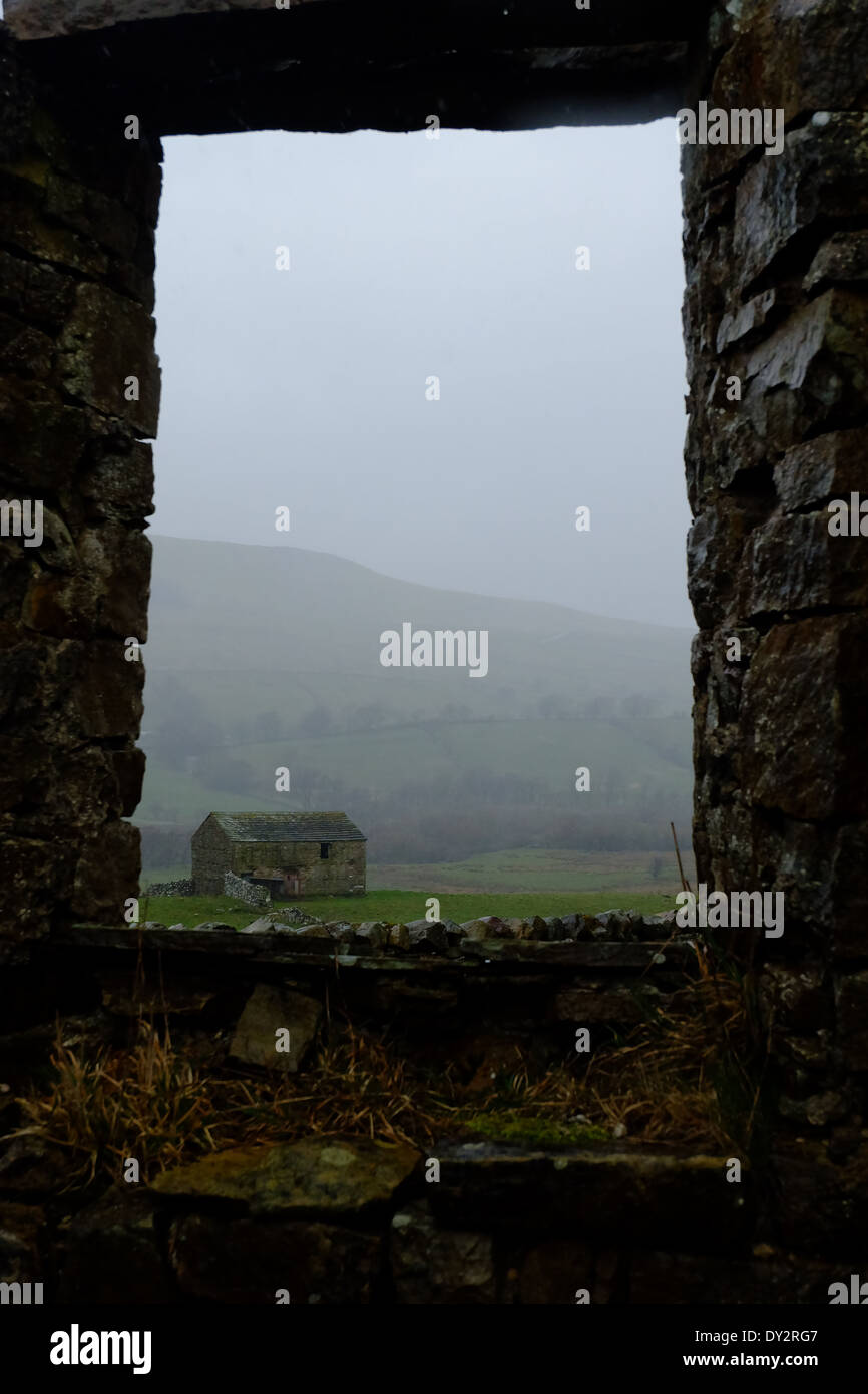 Stone barn, on a misty hill, framed by the ruin window of an old church. Stock Photo