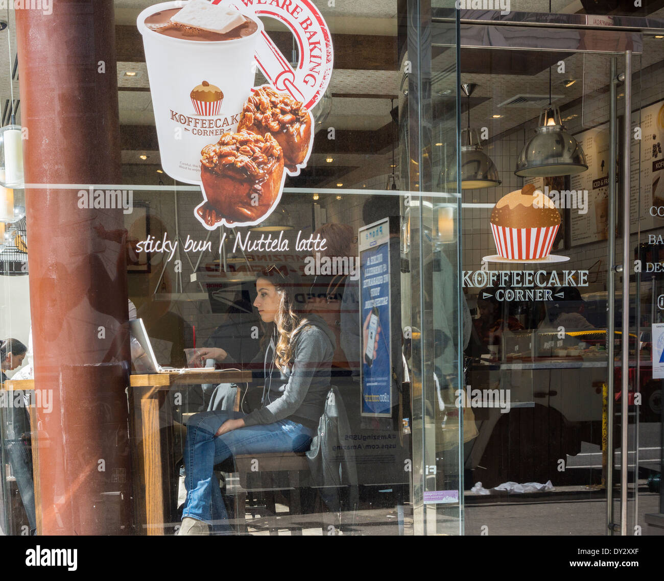 A woman works on her laptop in the window of a Koffeecake Corner coffee shop and bakery cafe in New York Stock Photo