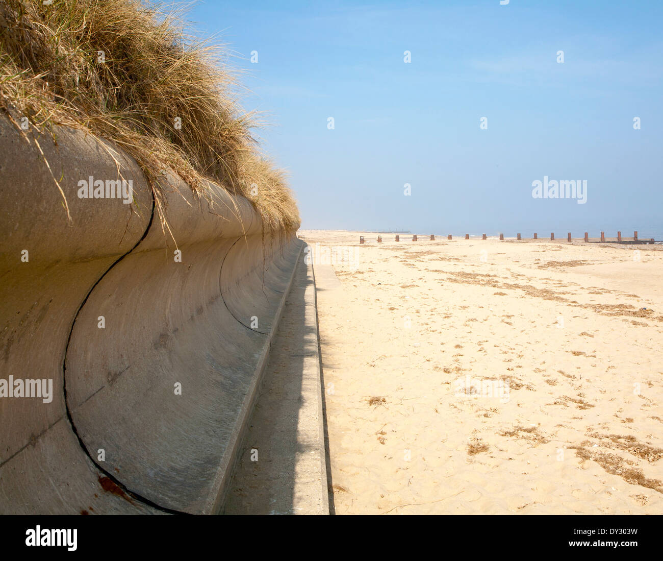 Wave return wall coastal defence and wide sandy beach submerging wooden groyne, Horsey, Norfolk, England Stock Photo