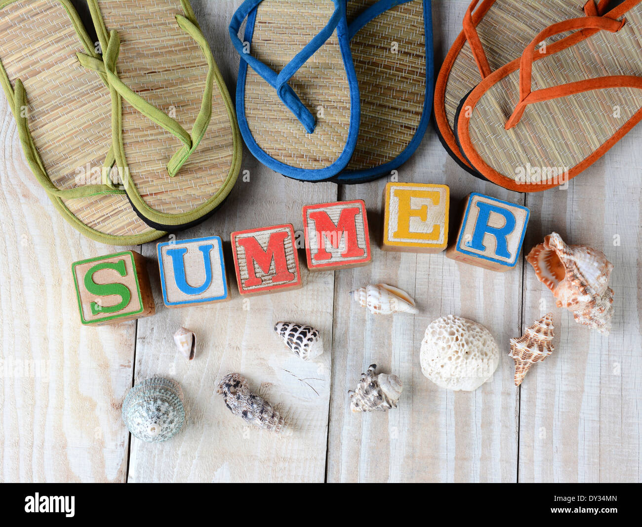 Childrens blocks spelling out Summer on rustic wooden boards The word is surrounded by sea shells, and flip-flop style sandals. Stock Photo