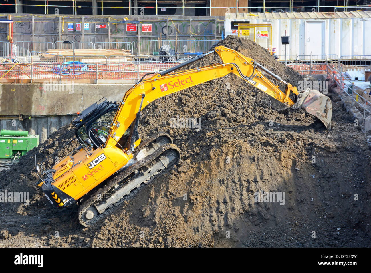 J.C. Bamford JCB tracked excavator equipment machine at work climbing back up to top of spoil heap on building construction site London England UK Stock Photo