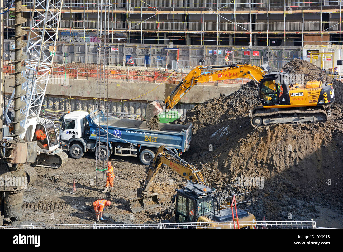 Steel cage being inserted into wet concrete pile (Continuous Flight Auger type) with JCB loading earth spoil into tipper lorry Stock Photo