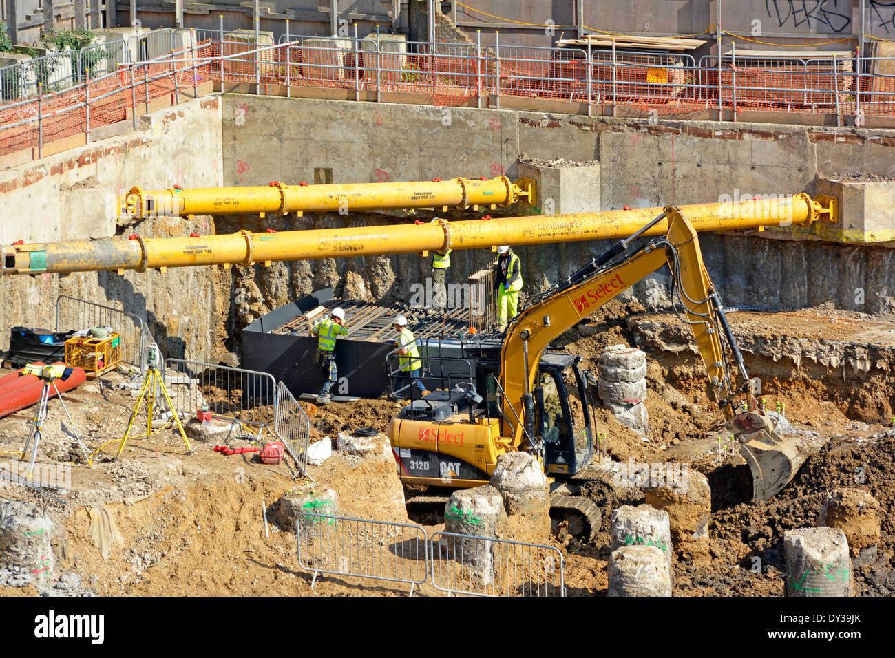 Construction building industry site workers below diagonal shoring struts across corners of concrete retaining wall digger excavating piles London UK Stock Photo