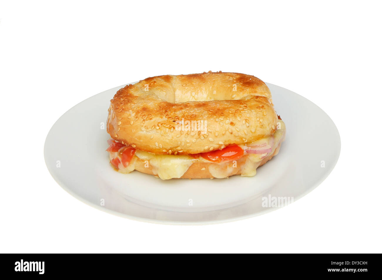 Toasted sesame seeded bagel filled with cheese, onion and tomato on a plate isolated against white Stock Photo