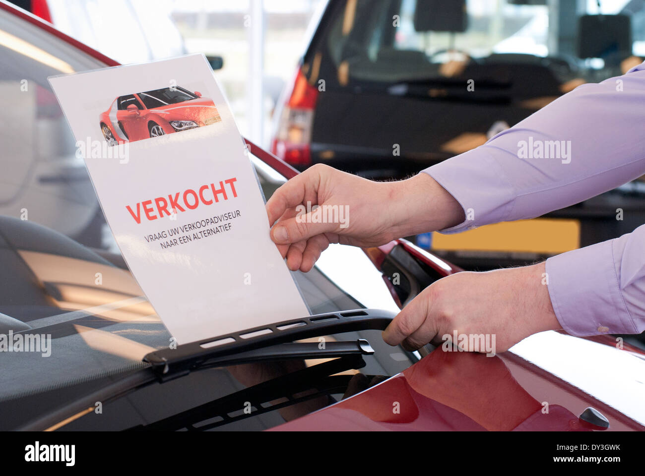 Car salesman puts a sold sign under the wiper of a car that is sold Stock Photo