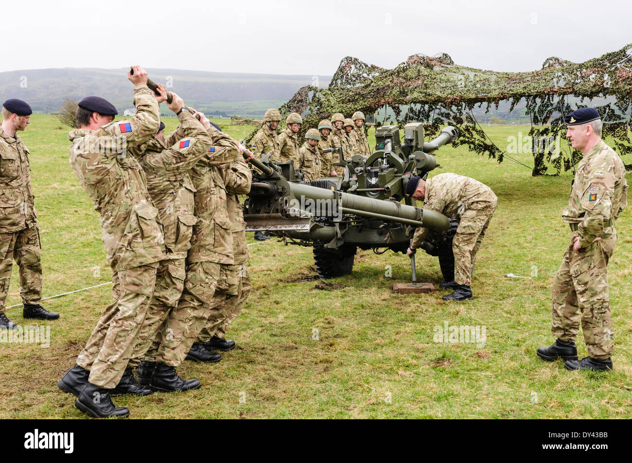 Soldiers from the Royal Artillery strain to lift a 105mm Light Artillery Gun to enable a colleague to prop up the wheels Stock Photo