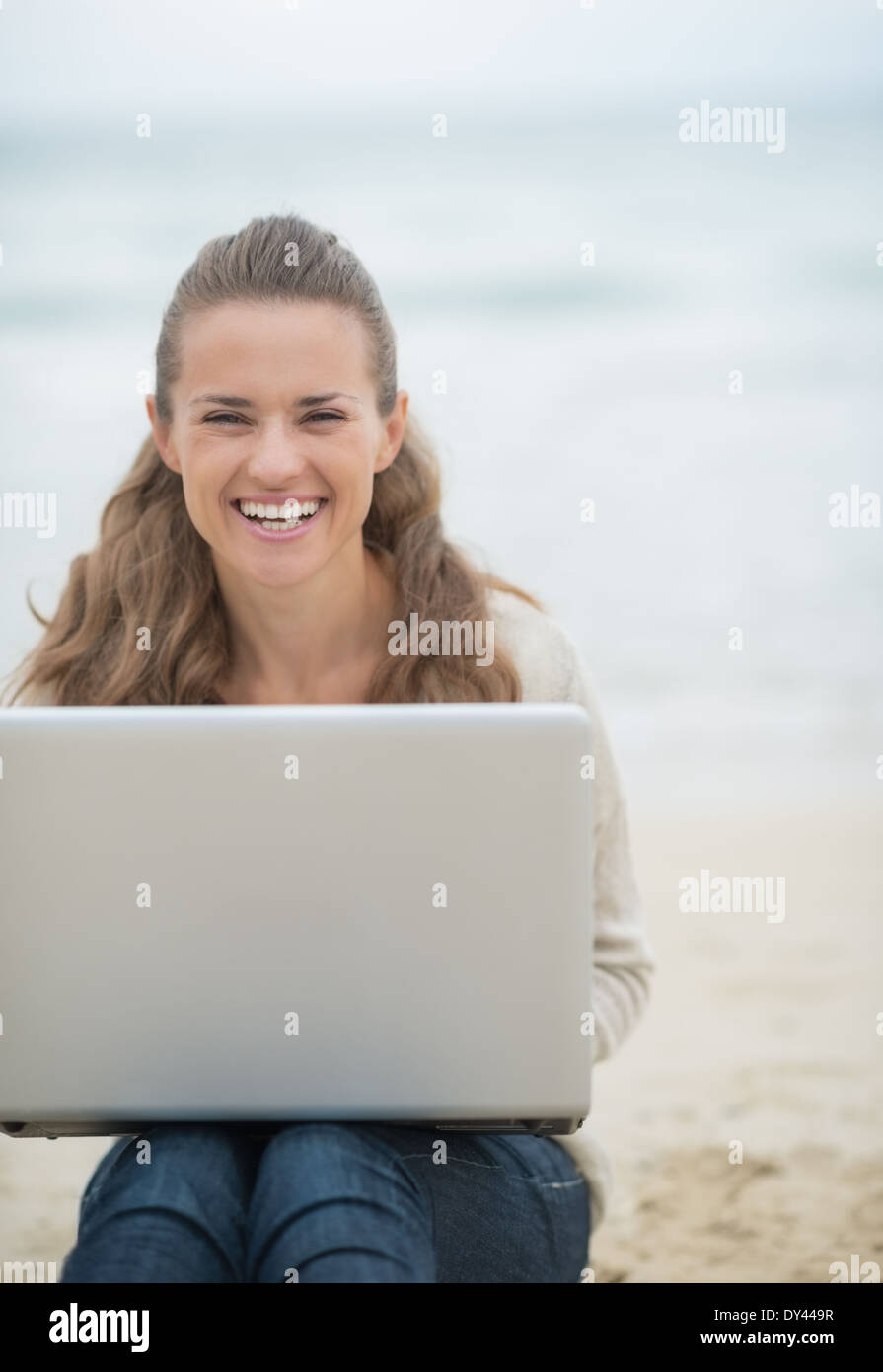 Happy young woman sitting with laptop on cold beach Stock Photo Alamy