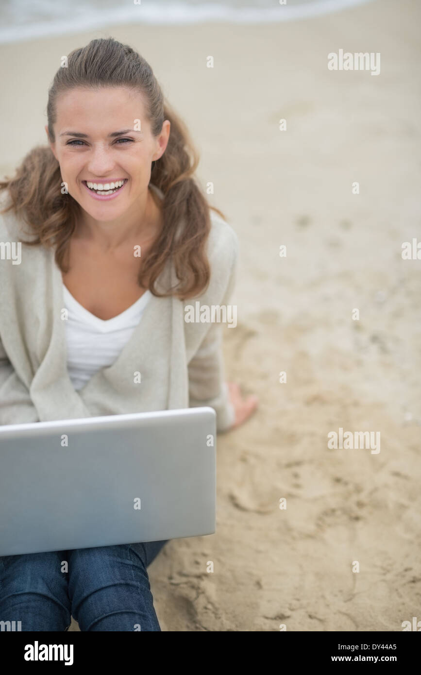 Happy young woman sitting with laptop on cold beach Stock Photo - Alamy