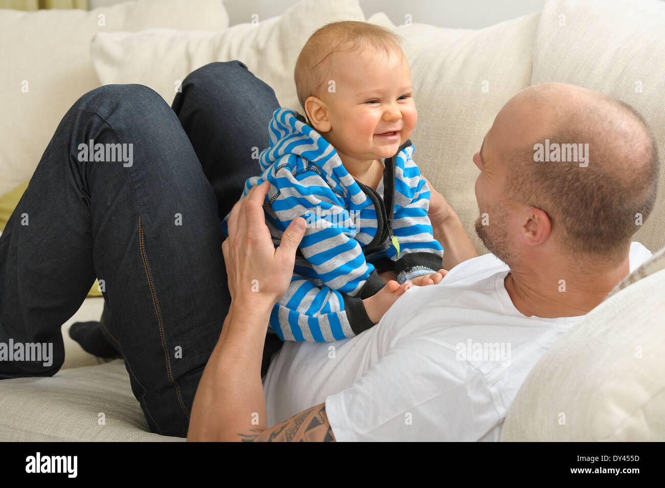 Father lying on a couch holds his baby son in his lap Stock Photo