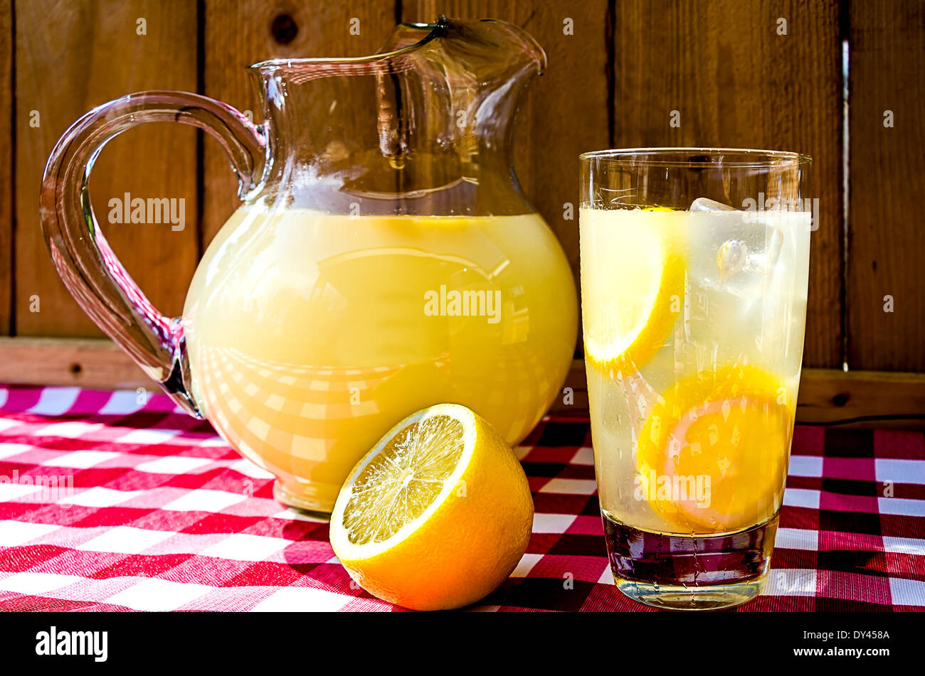 Lemonade and pitcher with sliced lemons on red gingham table cloth. Stock Photo