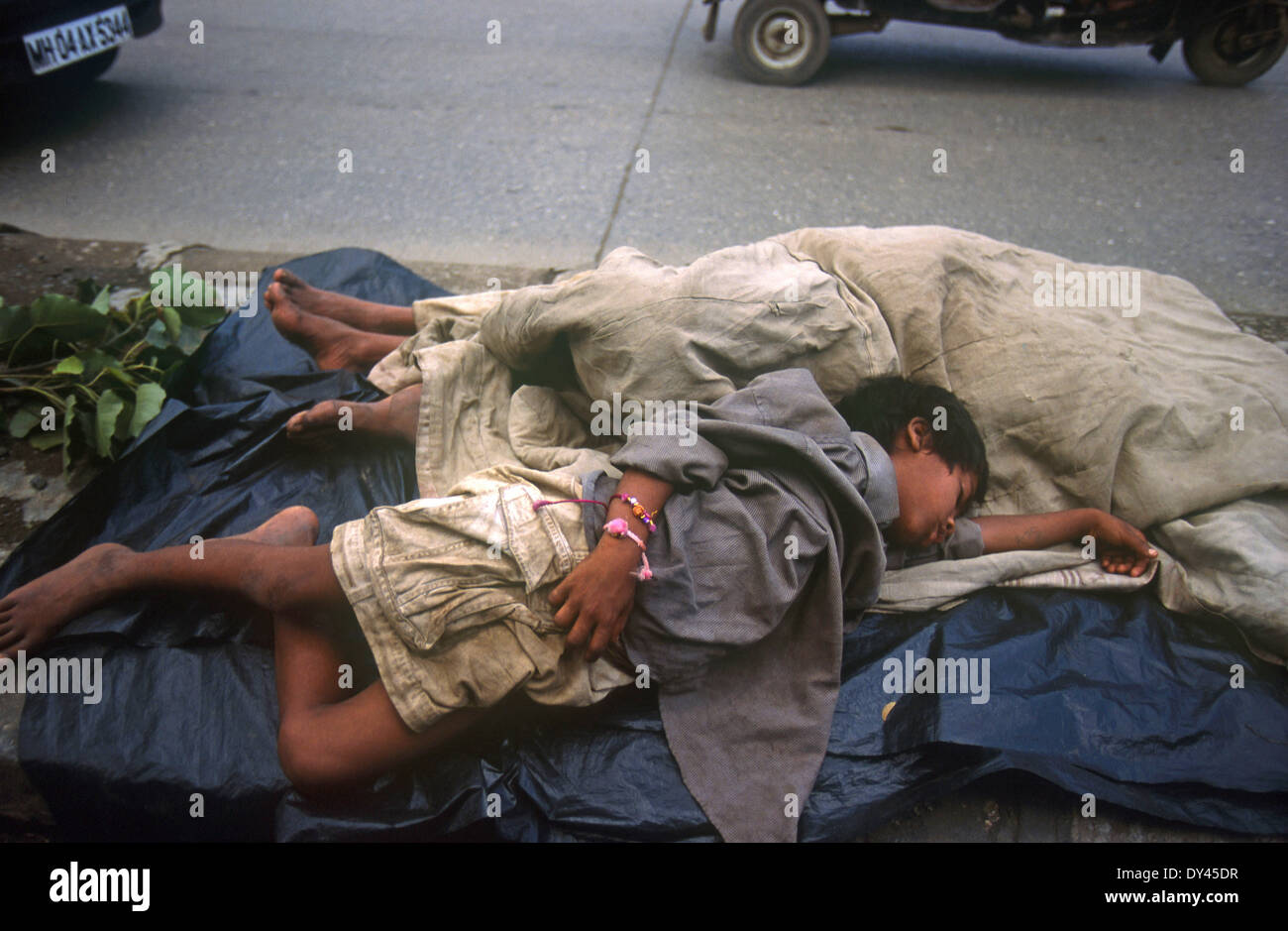 India Mumbai, street children sleep on the road beside traffic Stock