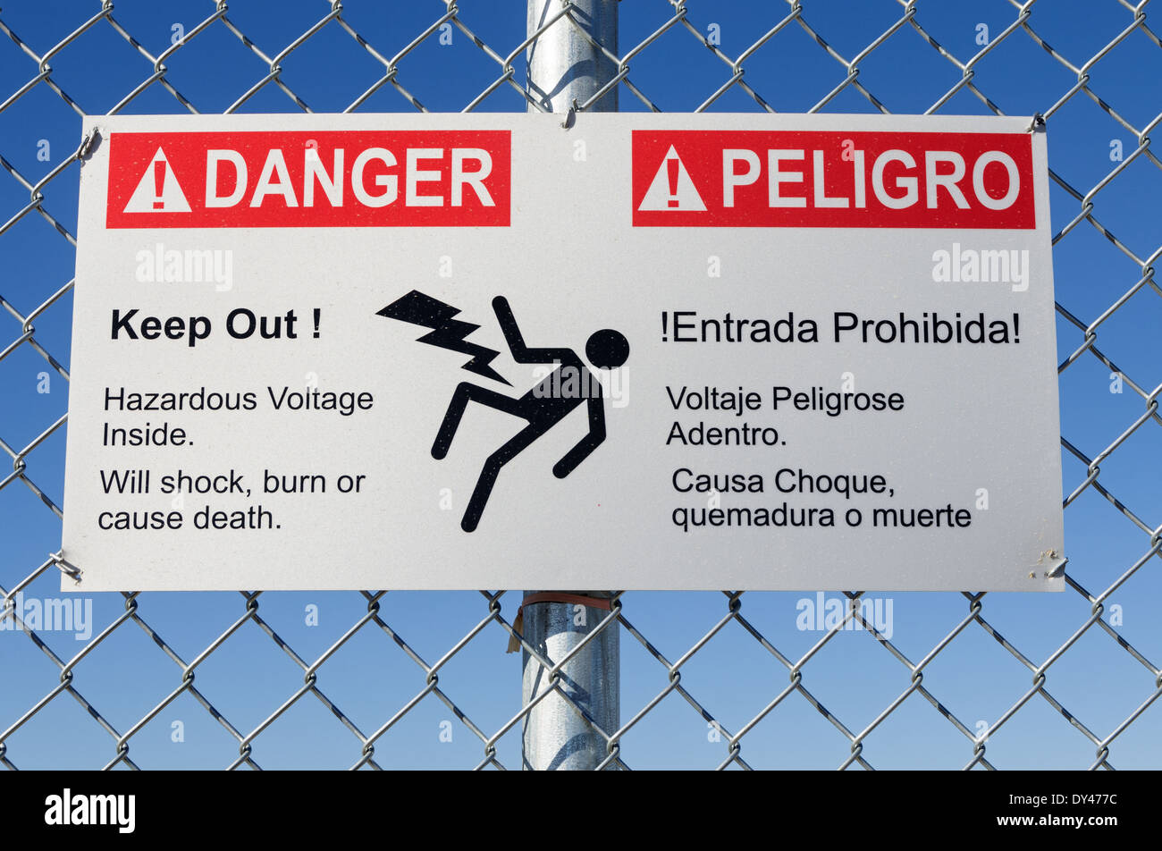 danger hazardous voltage keep out sign in English and Spanish on a fence with blue sky Stock Photo