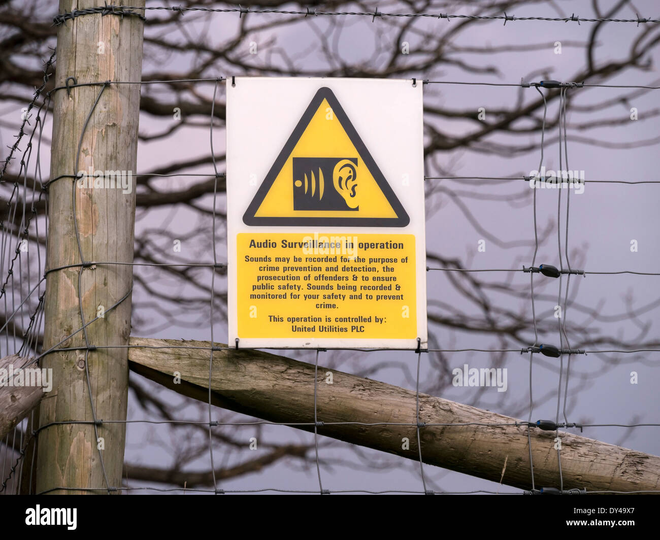 Unusual audio surveillance warning sign on fence around United Utilities water storage facility Stock Photo
