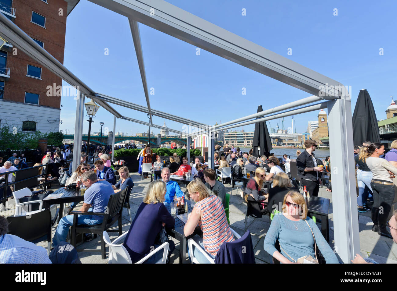 People taking advantage of the hot British weather to socialize with friends, drinking and eating by the Thames river, London. Stock Photo