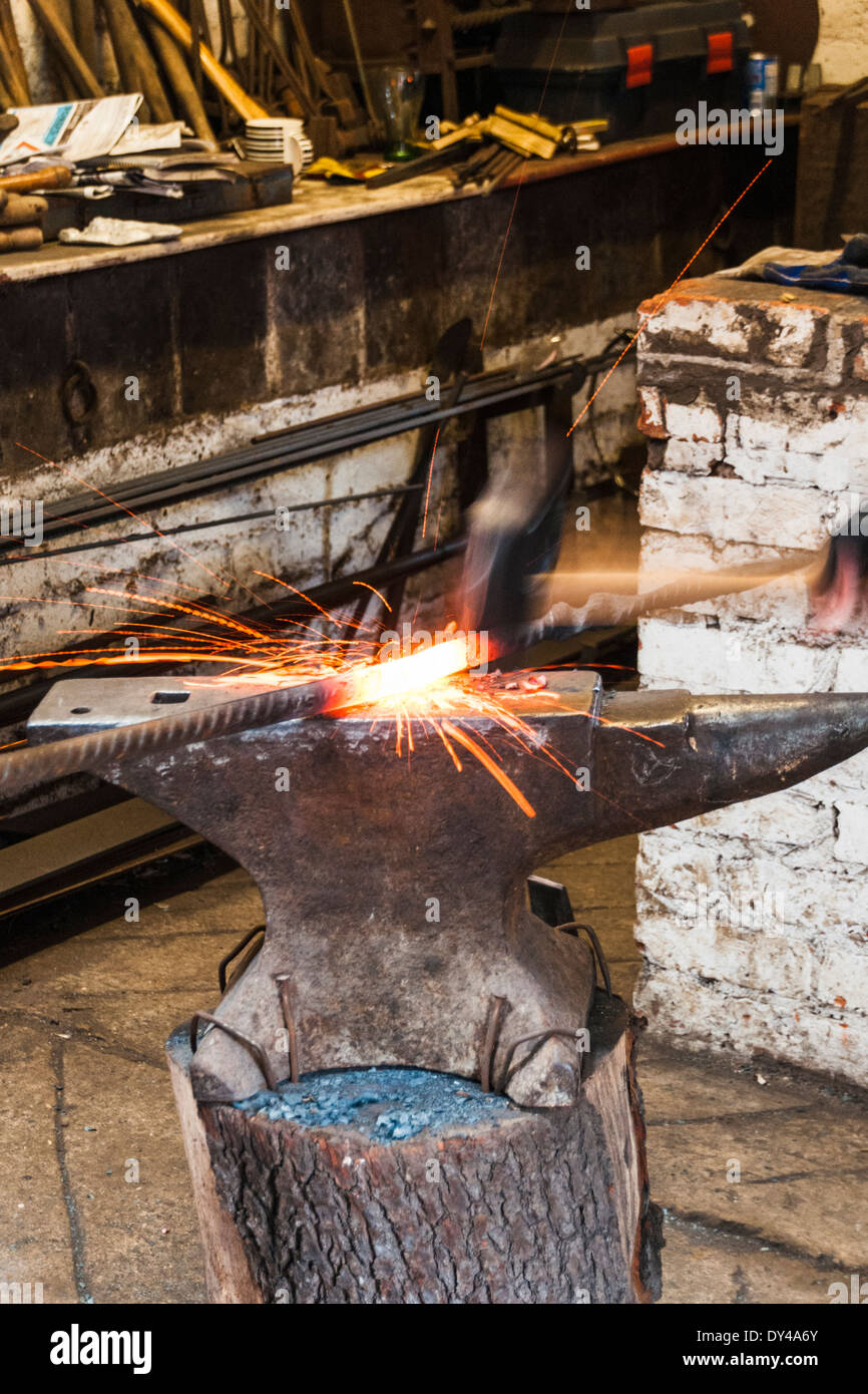 Blacksmiths hammer striking a red hot metal rod causing sparks to fly