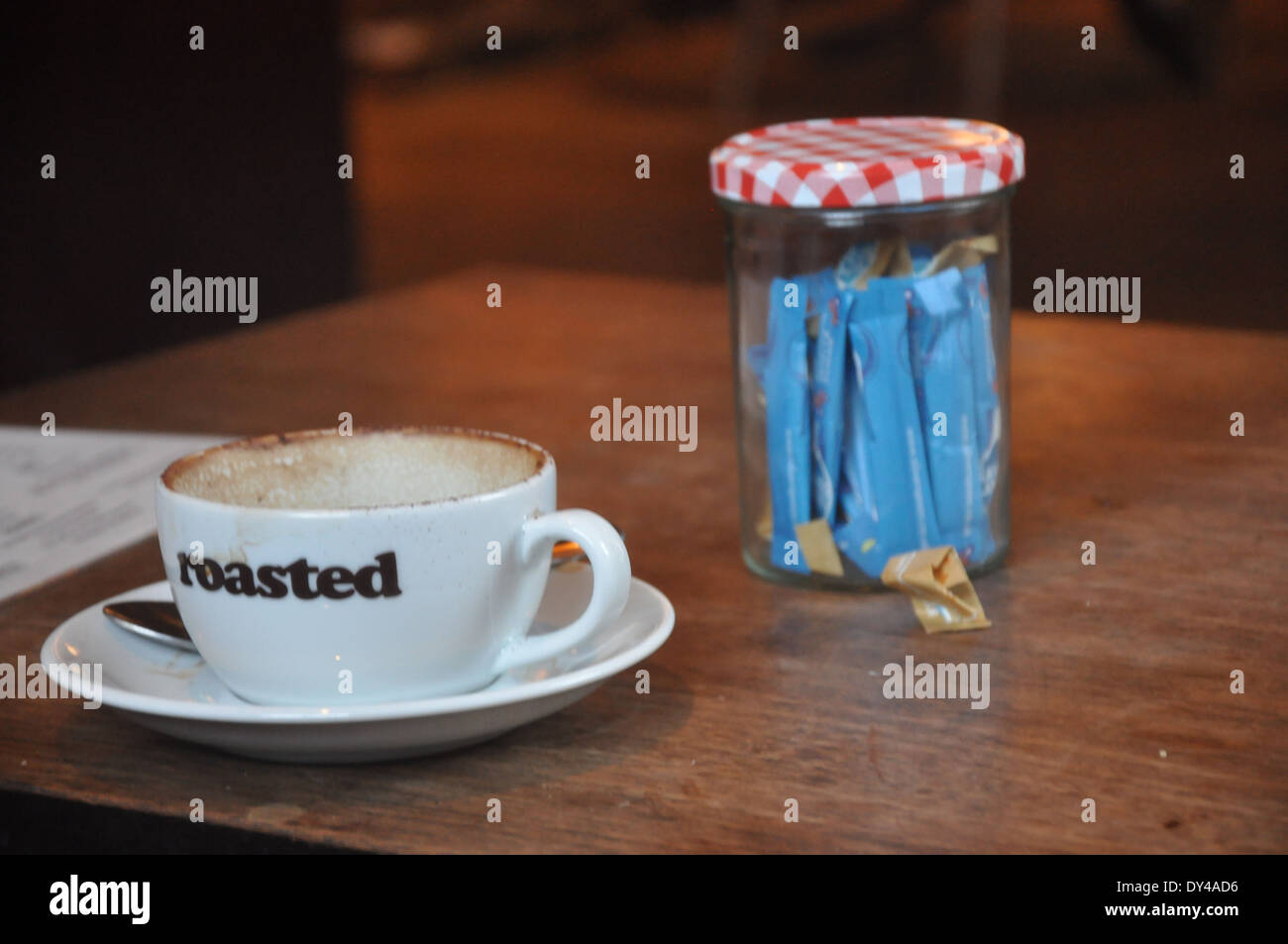 An empty coffee cup marked 'roasted' and jar of sugar portions on a wooden table Stock Photo