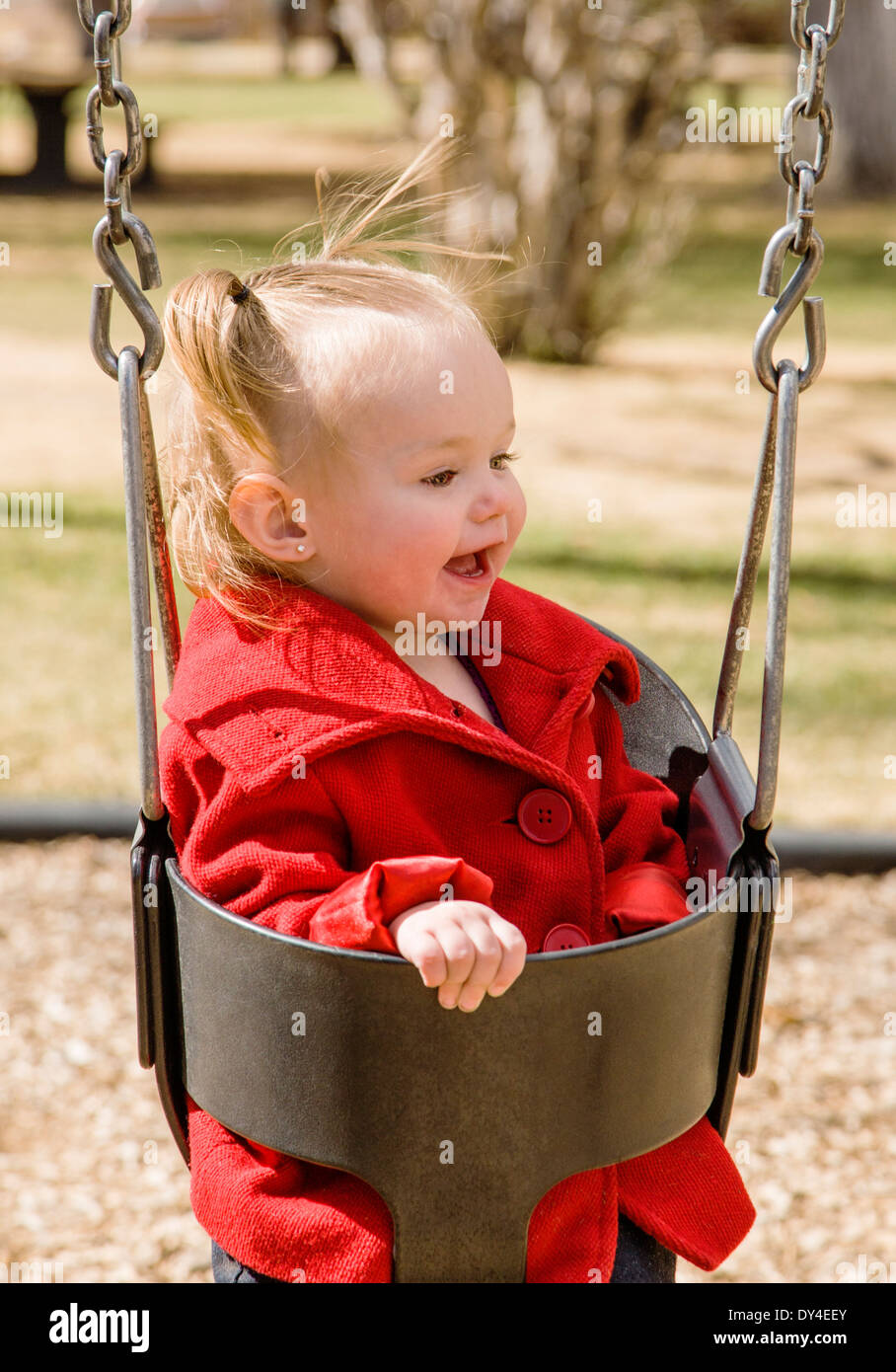 Adorable, cute 16 month little girl swinging on a park playground Stock Photo