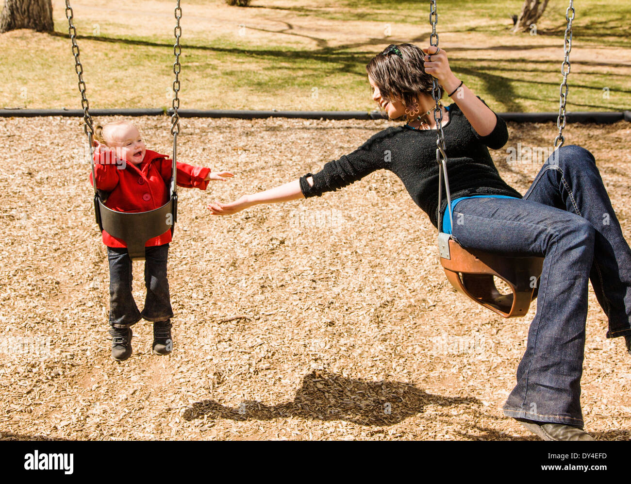 Beautiful young mother playing with adorable, cute 16 month baby girl on park playground swings Stock Photo