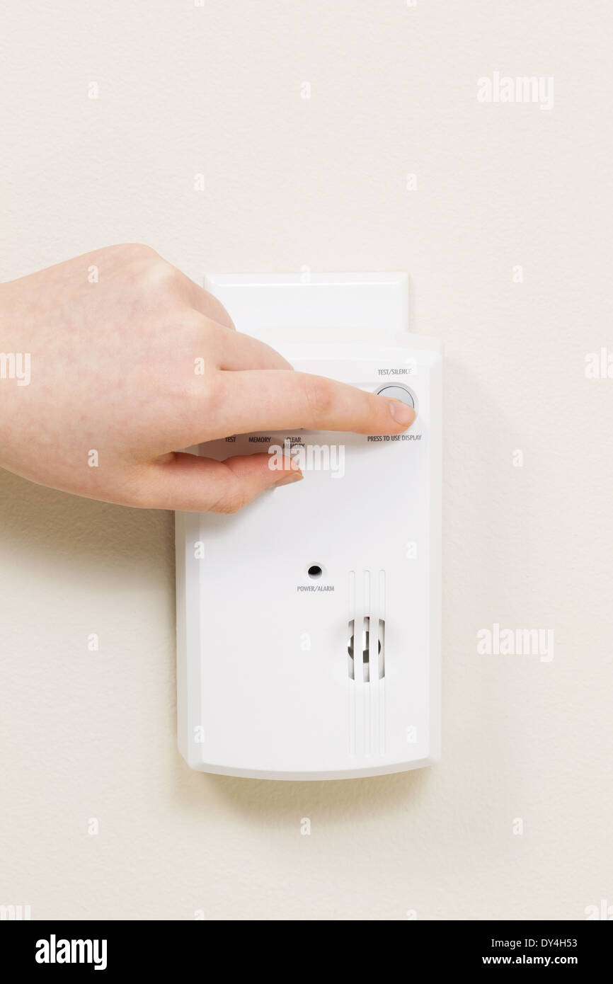 Vertical photo of carbon monoxide alarm with female hand testing the system Stock Photo