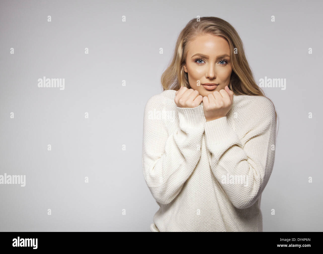 Portrait of beautiful young blond wearing sweater feeling cold. Cute young female fashion model posing on gray background. Stock Photo