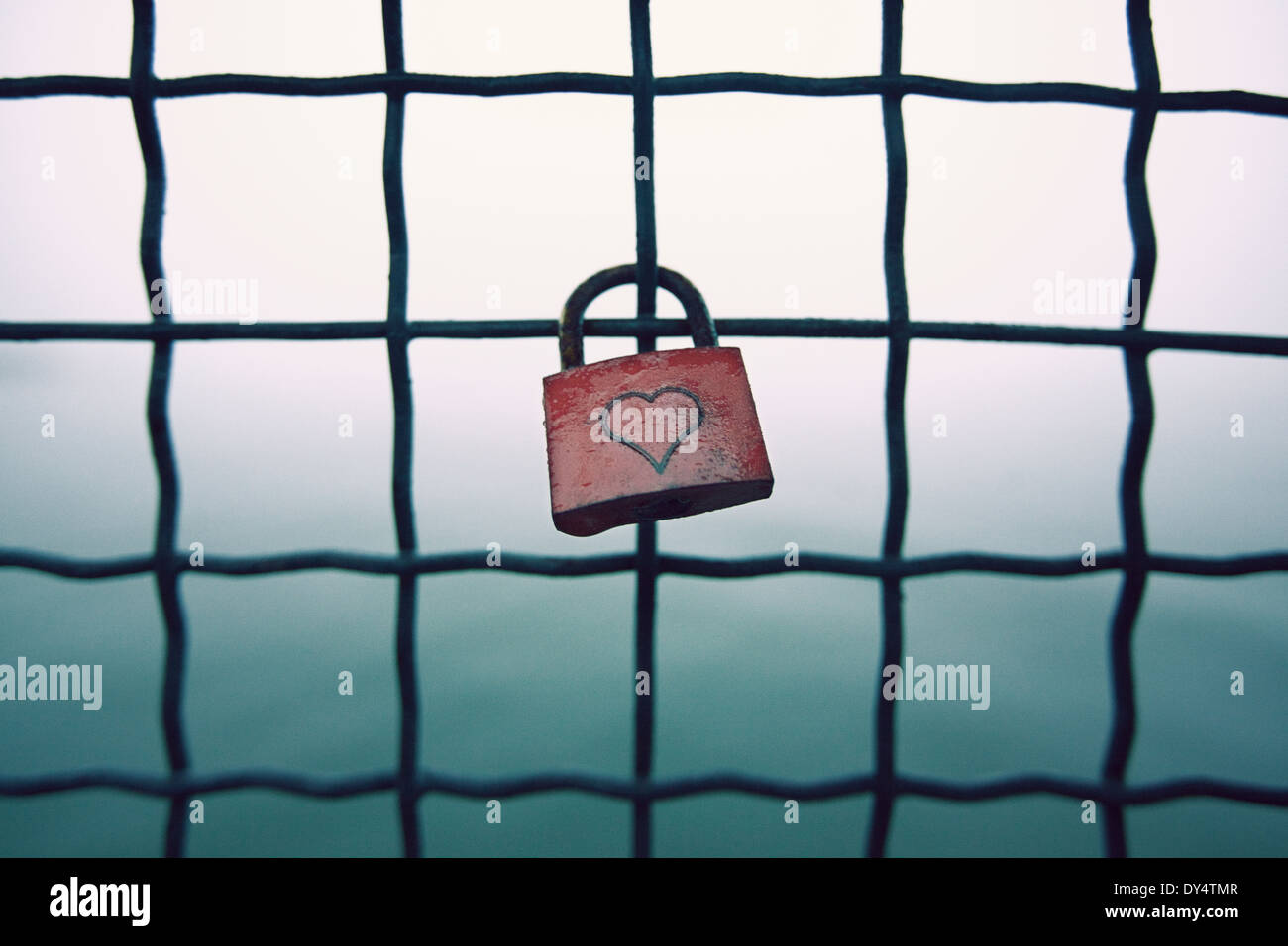 Red padlock with heart shape attached to wire fence Stock Photo