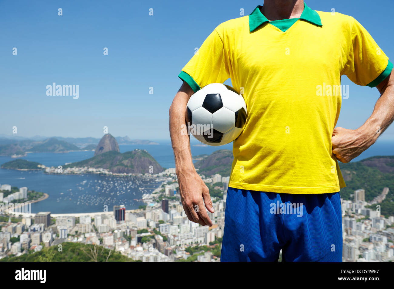 Brazilian soccer player holding football wearing kit in Brazil colors at bright sunny Rio de Janeiro skyline with Sugarloaf Stock Photo