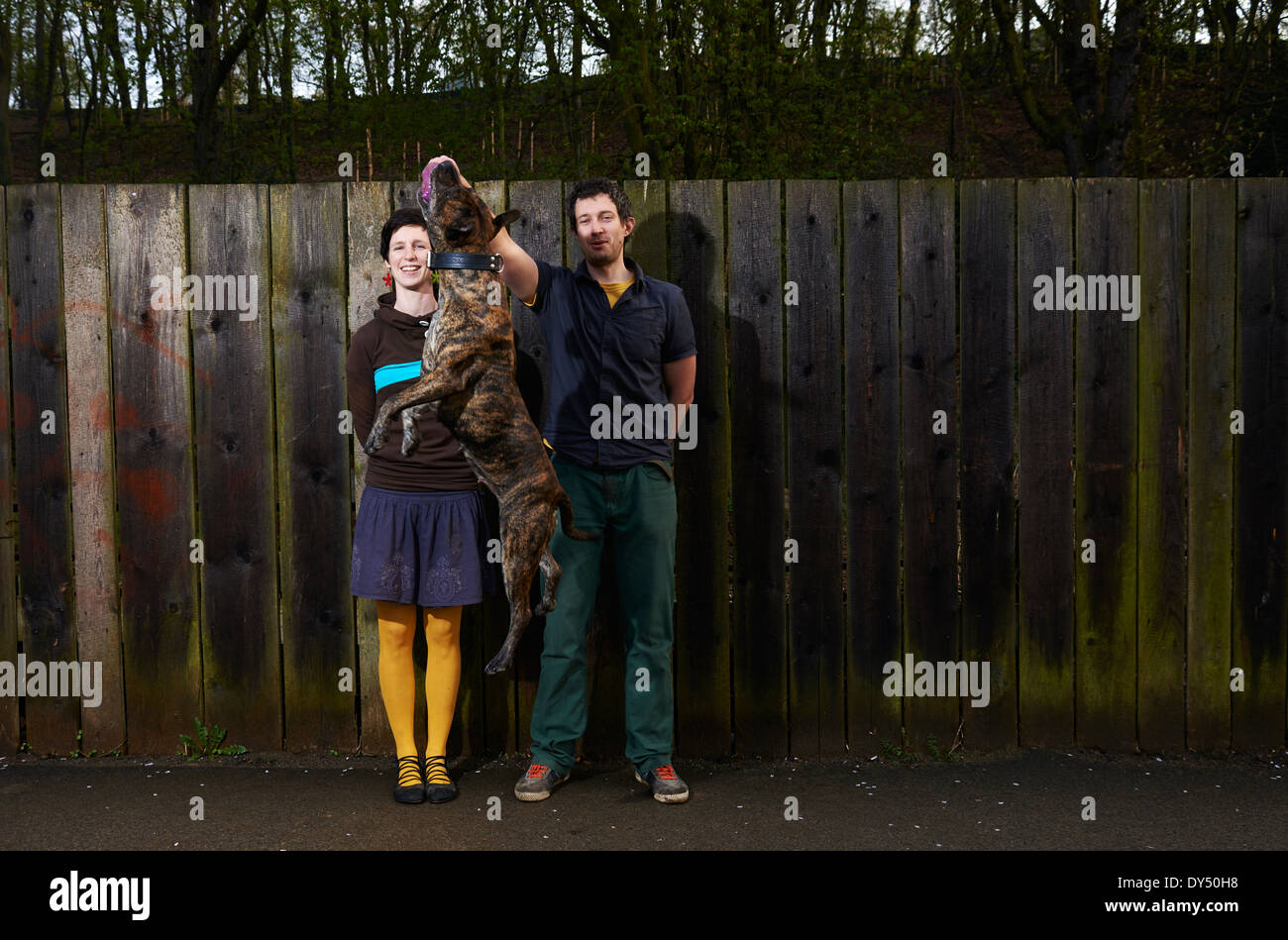 Happy Young Couple Playing with their jumping dog in the Park standing ...