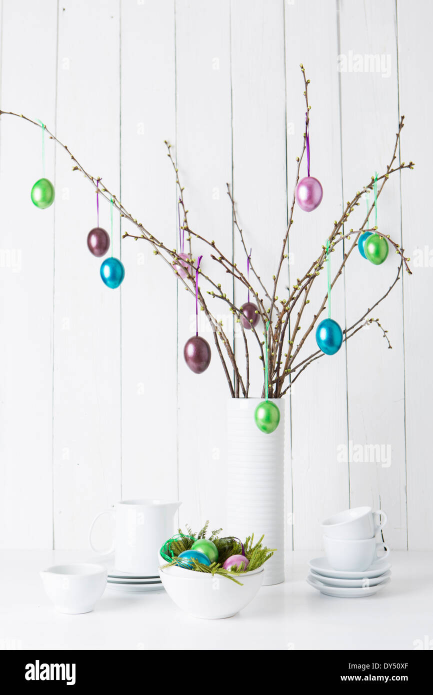 Still life of crockery and shiny easter eggs hanging from twigs Stock Photo