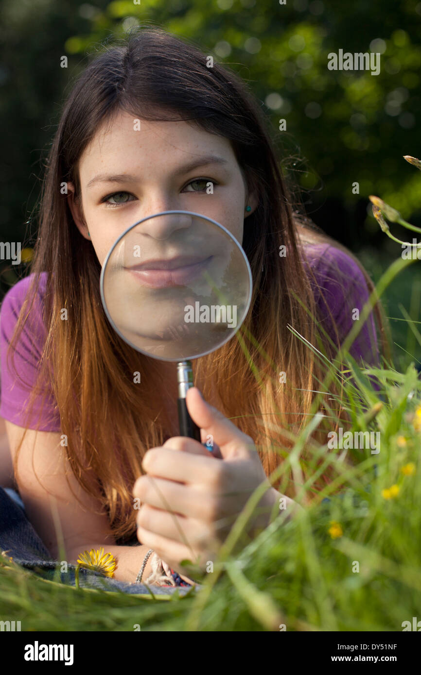 Teenage girl lying in grass holding up a magnifying glass to her mouth Stock Photo