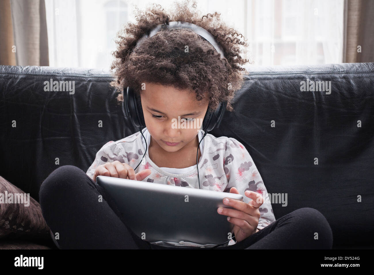 Girl sitting on sofa using digital tablet and headphones Stock Photo