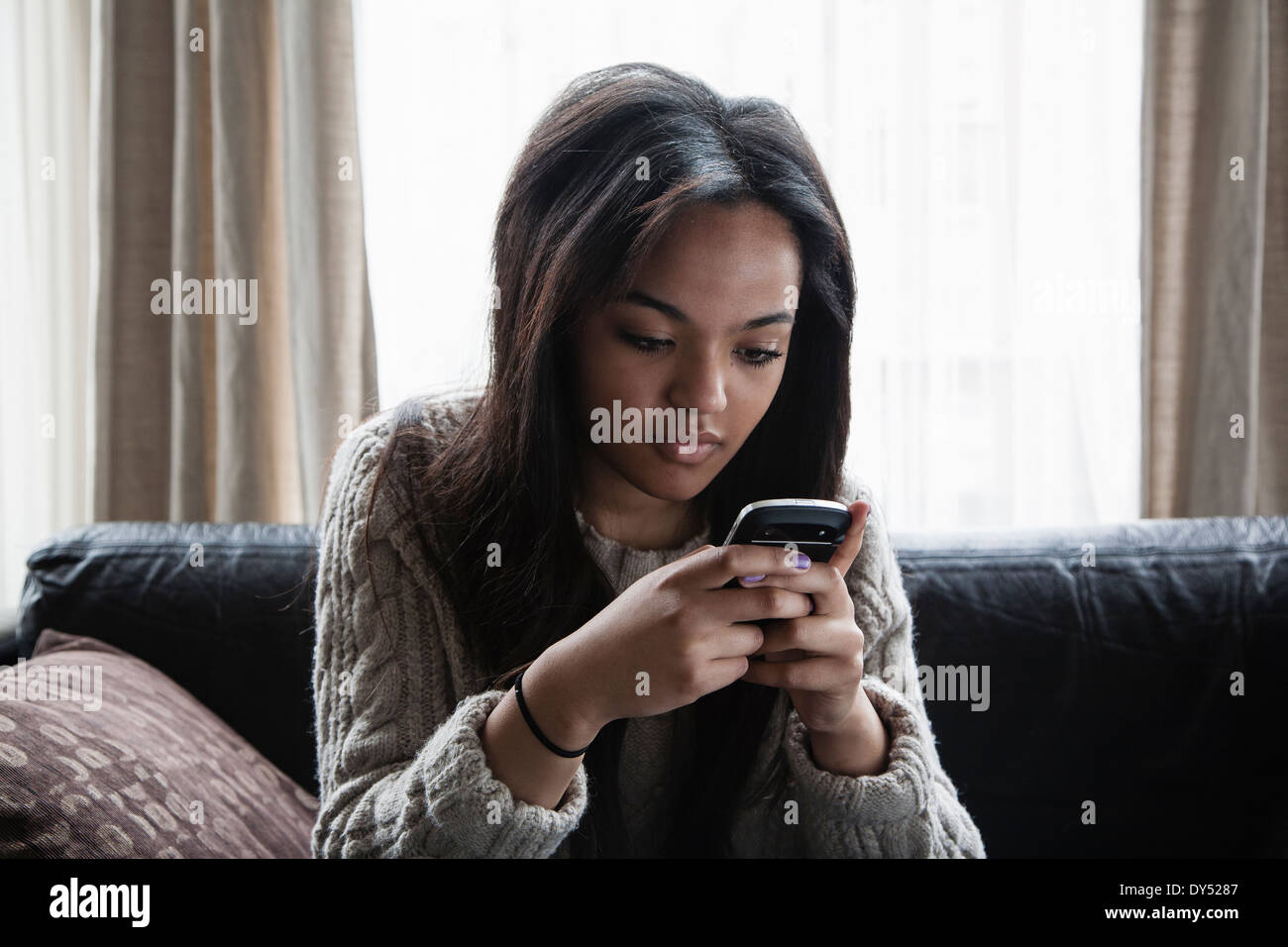 Teenage girl sitting on sofa texting on smartphone Stock Photo
