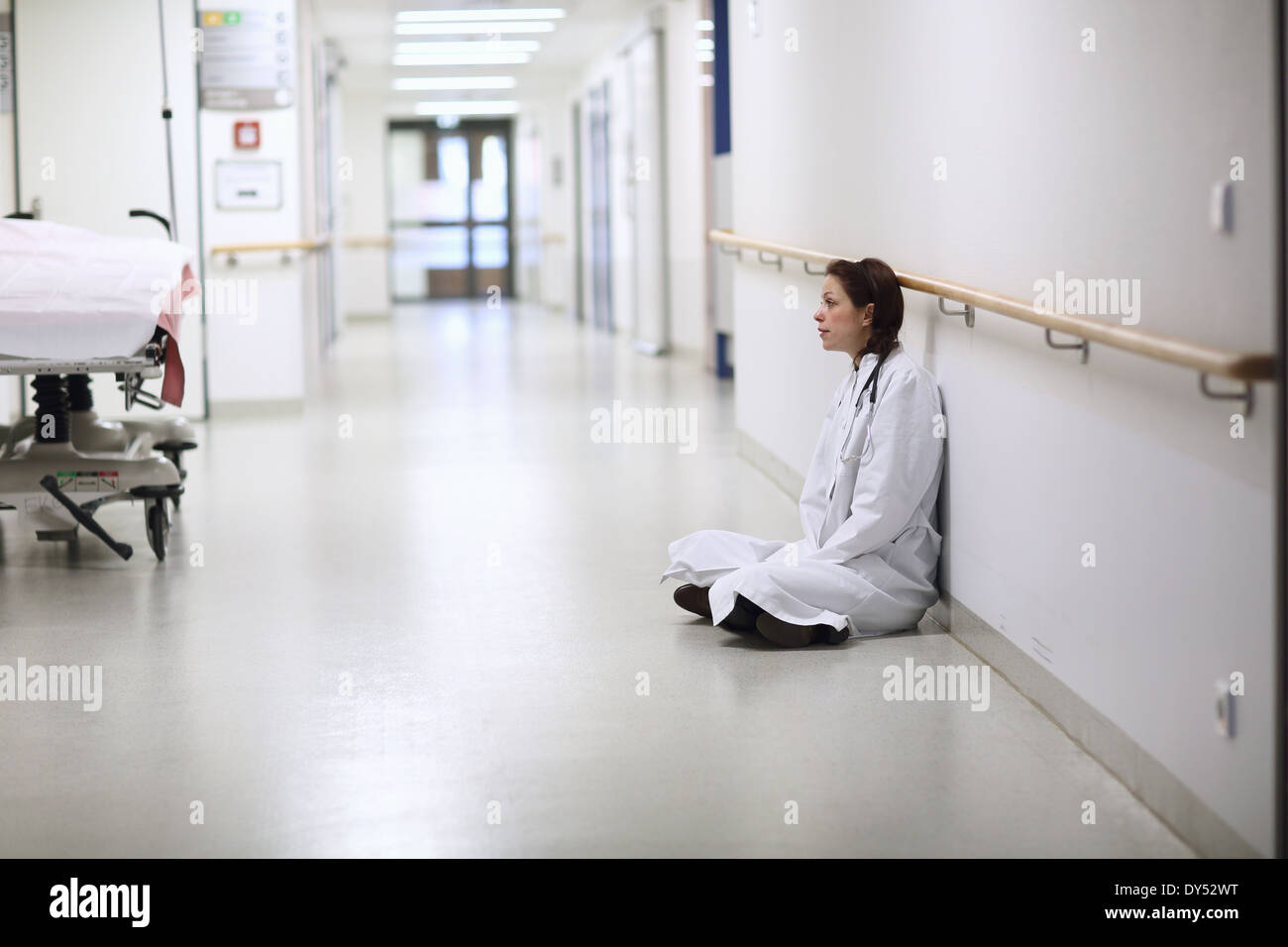 Female doctor sitting cross legged in hospital corridor Stock Photo