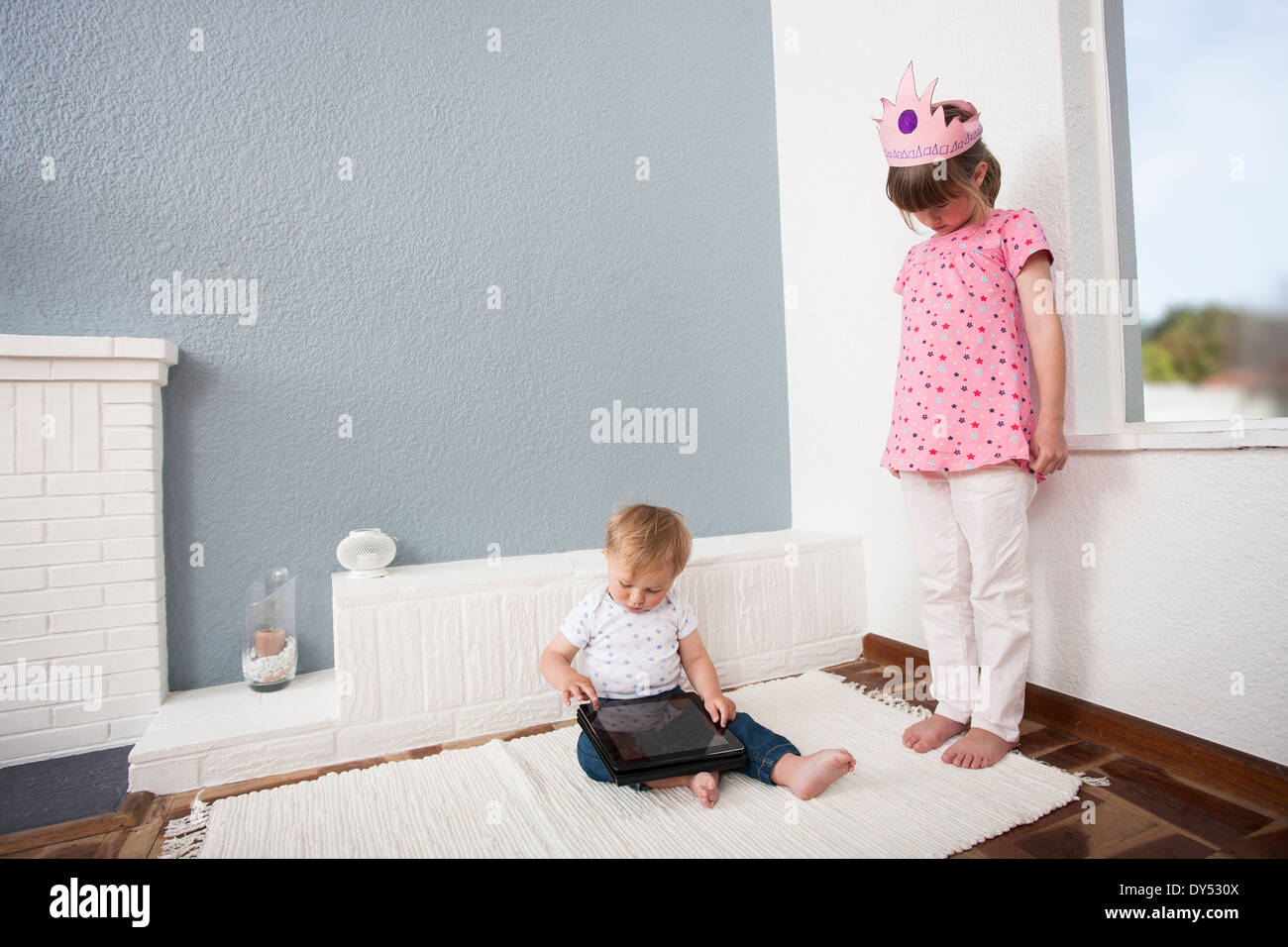 Girl watching over baby boy playing digital tablet Stock Photo