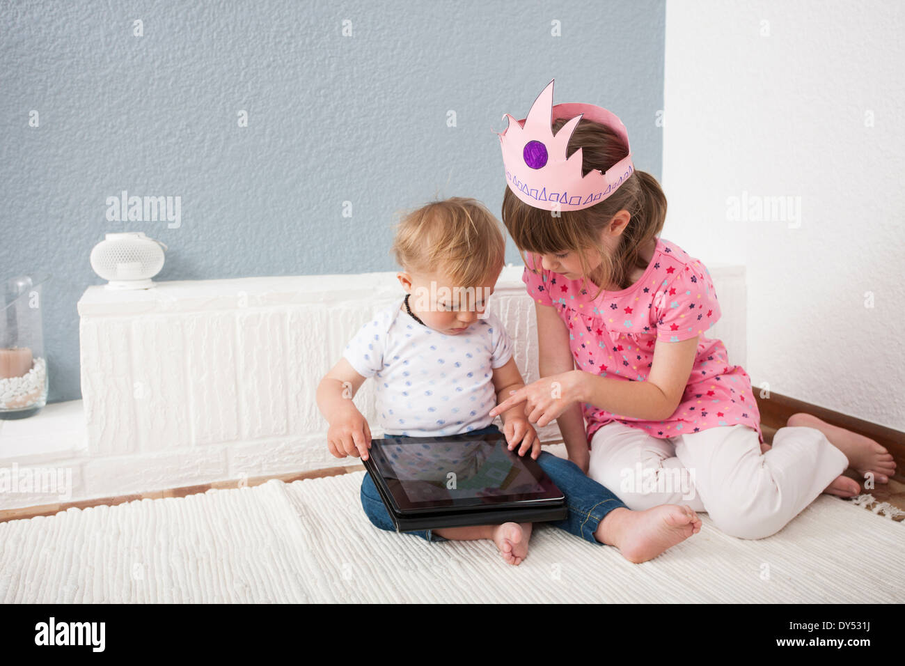 Girl watching over baby boy playing digital tablet Stock Photo