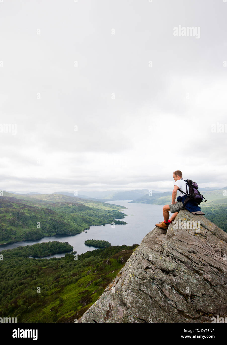 hillwalker sitting on a rock at the top of Ben A'An, in Scotland, looking down at Loch Katrine Stock Photo