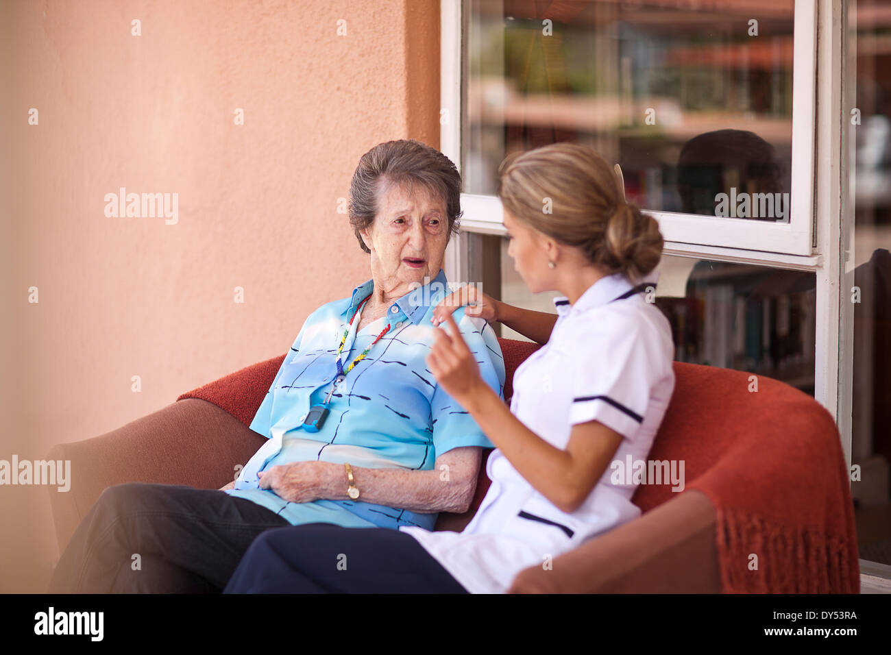 Care assistant chatting to senior woman on sofa Stock Photo