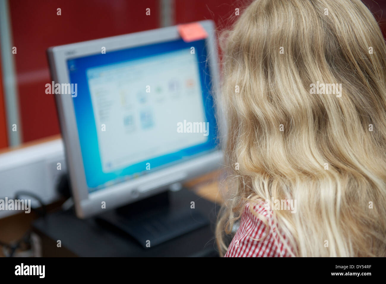 A young blonde UK british schoolgirl sitting at a desktop PC in an ICT lesson Stock Photo