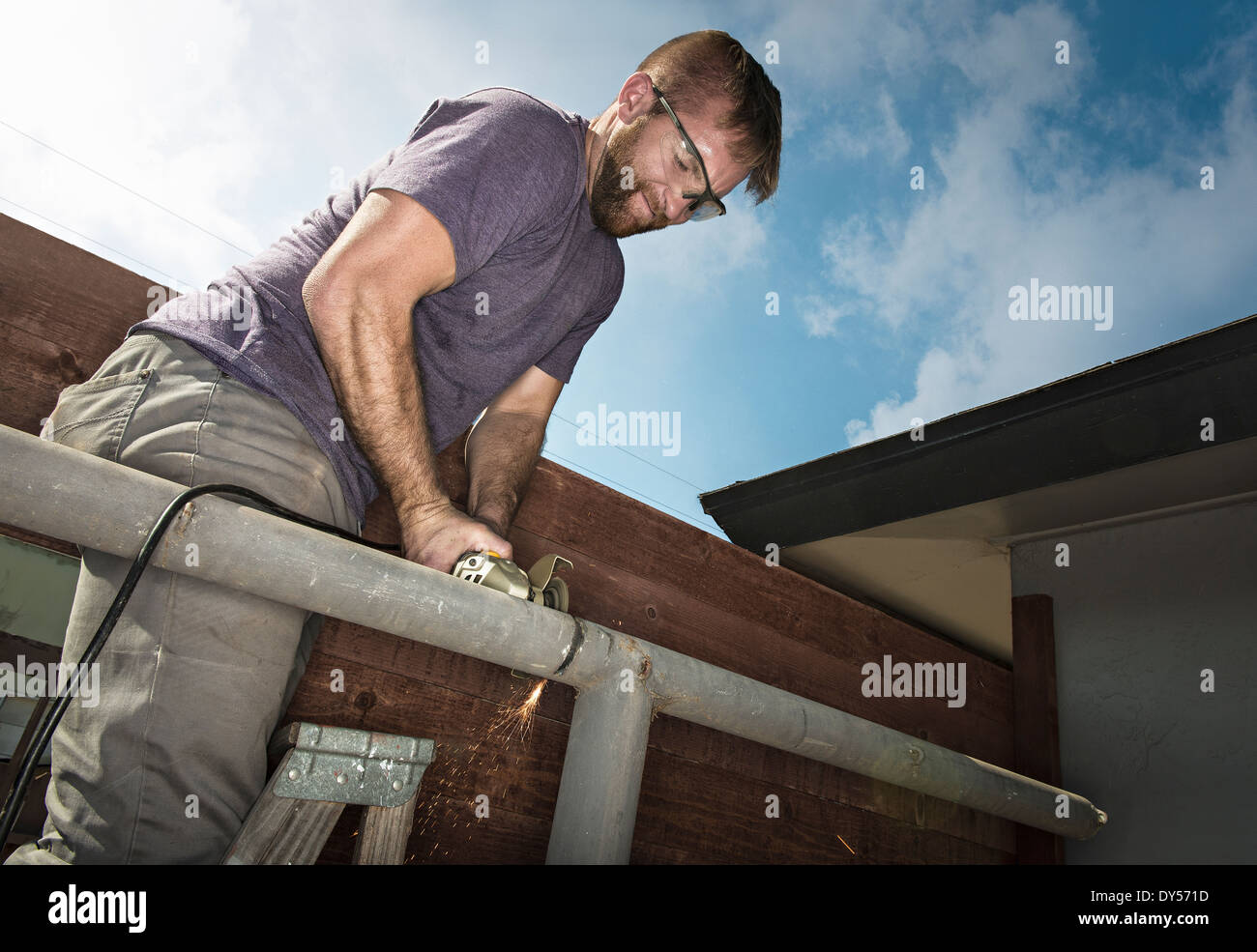 Builder on ladder sawing metal piping Stock Photo