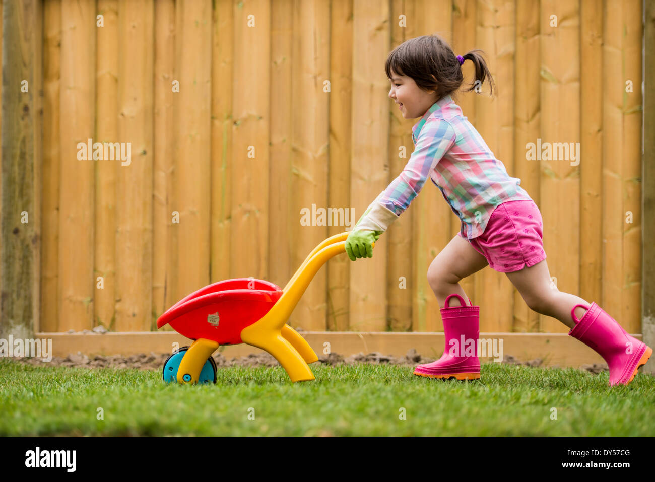 Young girl running with toy wheelbarrow in the garden Stock Photo