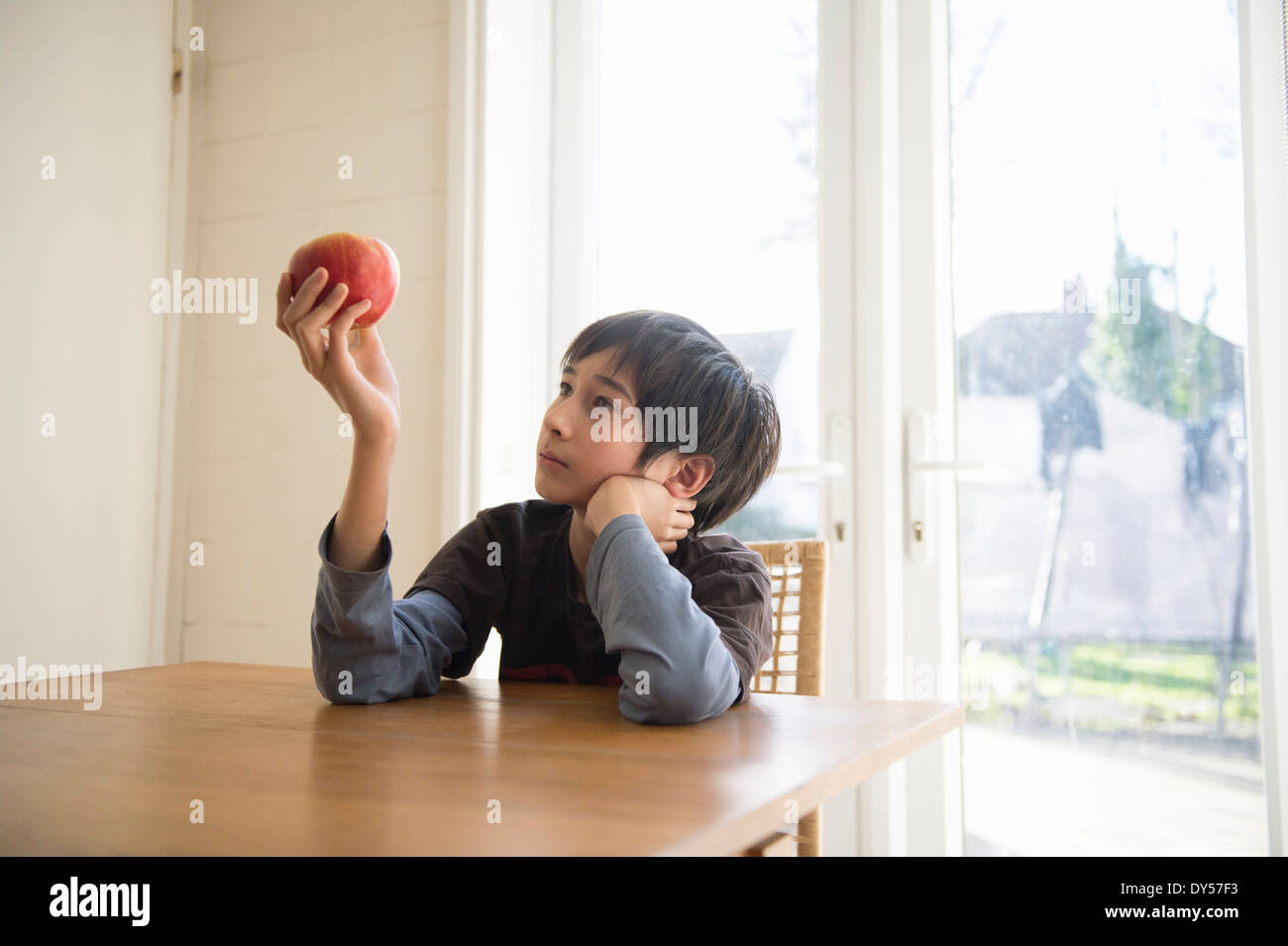 Boy sitting at table, holding an apple in front of him Stock Photo