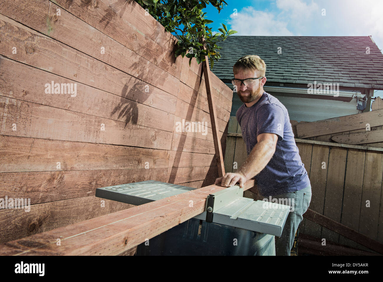 Joiner in backyard measuring planks of wood on workbench Stock Photo