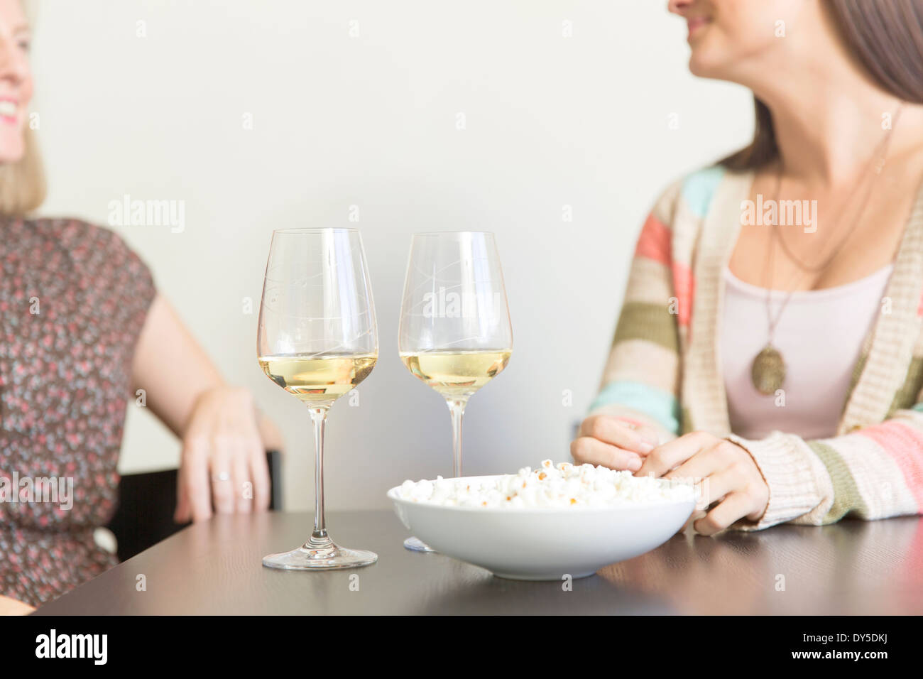 Mid adult female friends drinking at table with wine and popcorn Stock Photo