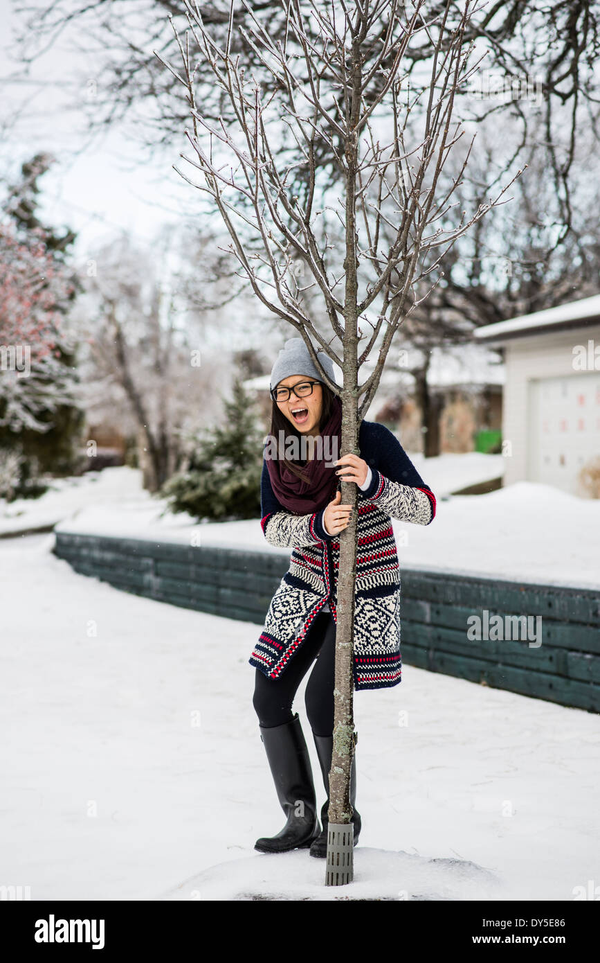 Young woman holding onto tree in slippy snow Stock Photo
