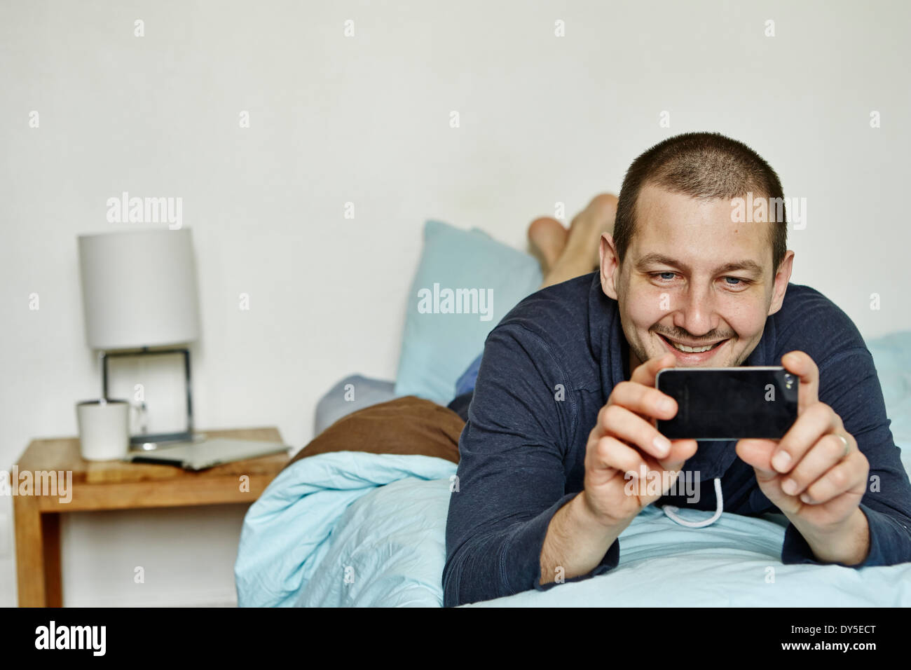 Mid adult man lying on bed taking self portrait on cellphone Stock Photo