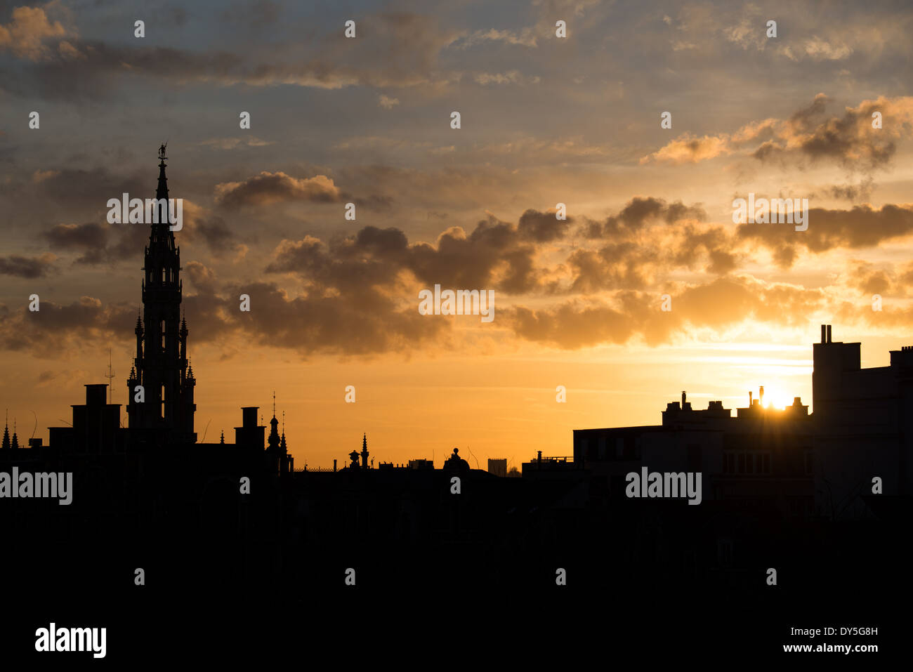 The silhouette of Brussels skyline at sunset against a golden sky with a few clouds. The tall spire is the tower of the Brussels Town Hall (Hotel de Ville) standing at 96 meters. Stock Photo