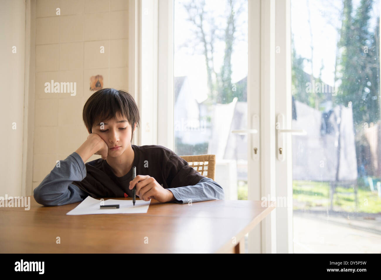 Boy sitting at table, holding pen to paper Stock Photo