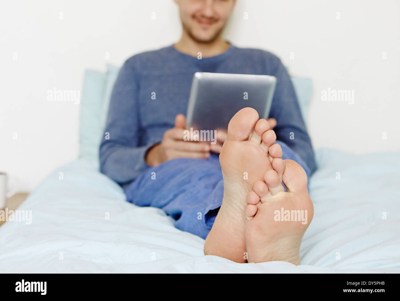 Mid adult man lying on bed using digital tablet Stock Photo